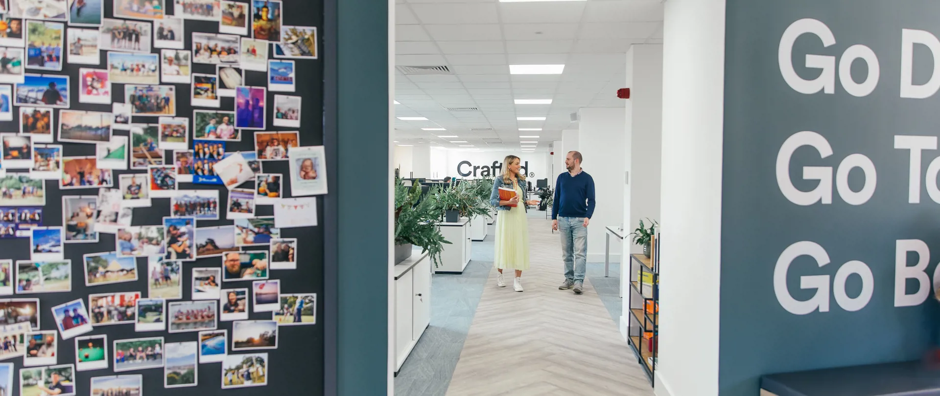 Two Crafted team members walking through the office next to a photo wall montage of social events
