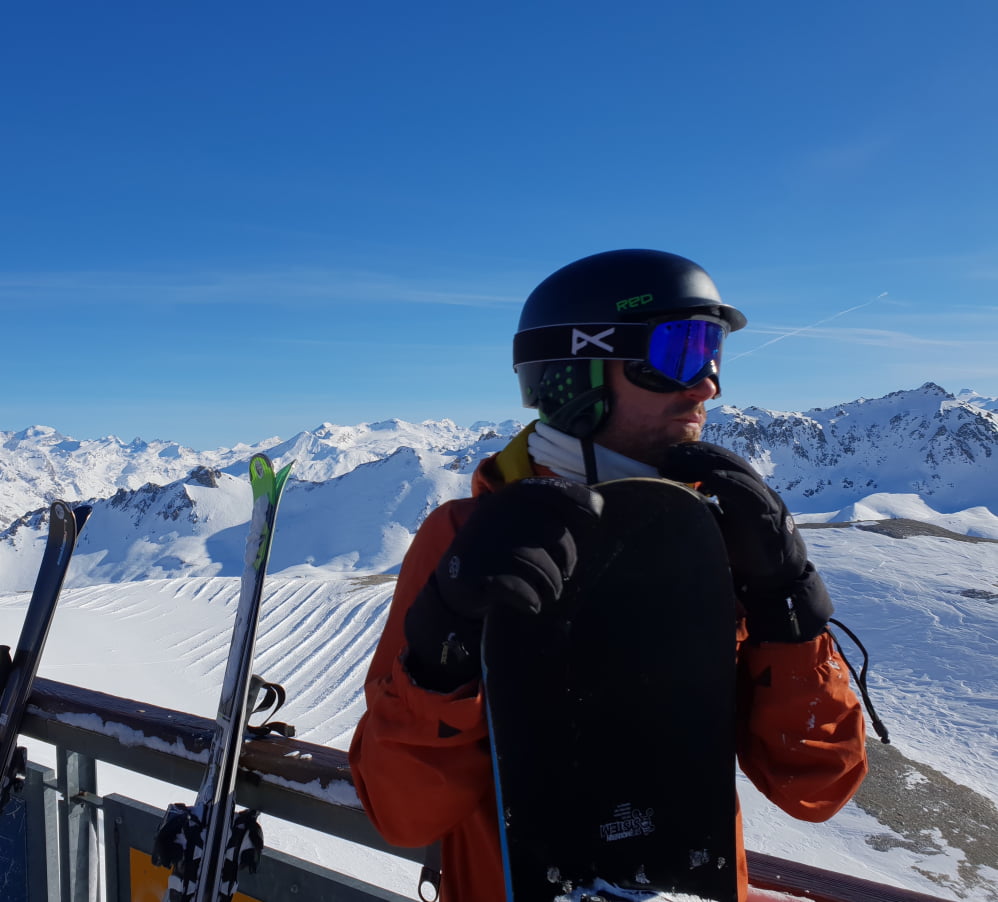 A person wearing ski goggles and a helmet with snow covered mountains behind.