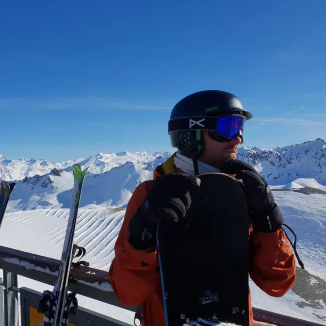 A person wearing ski goggles and a helmet with snow covered mountains behind.