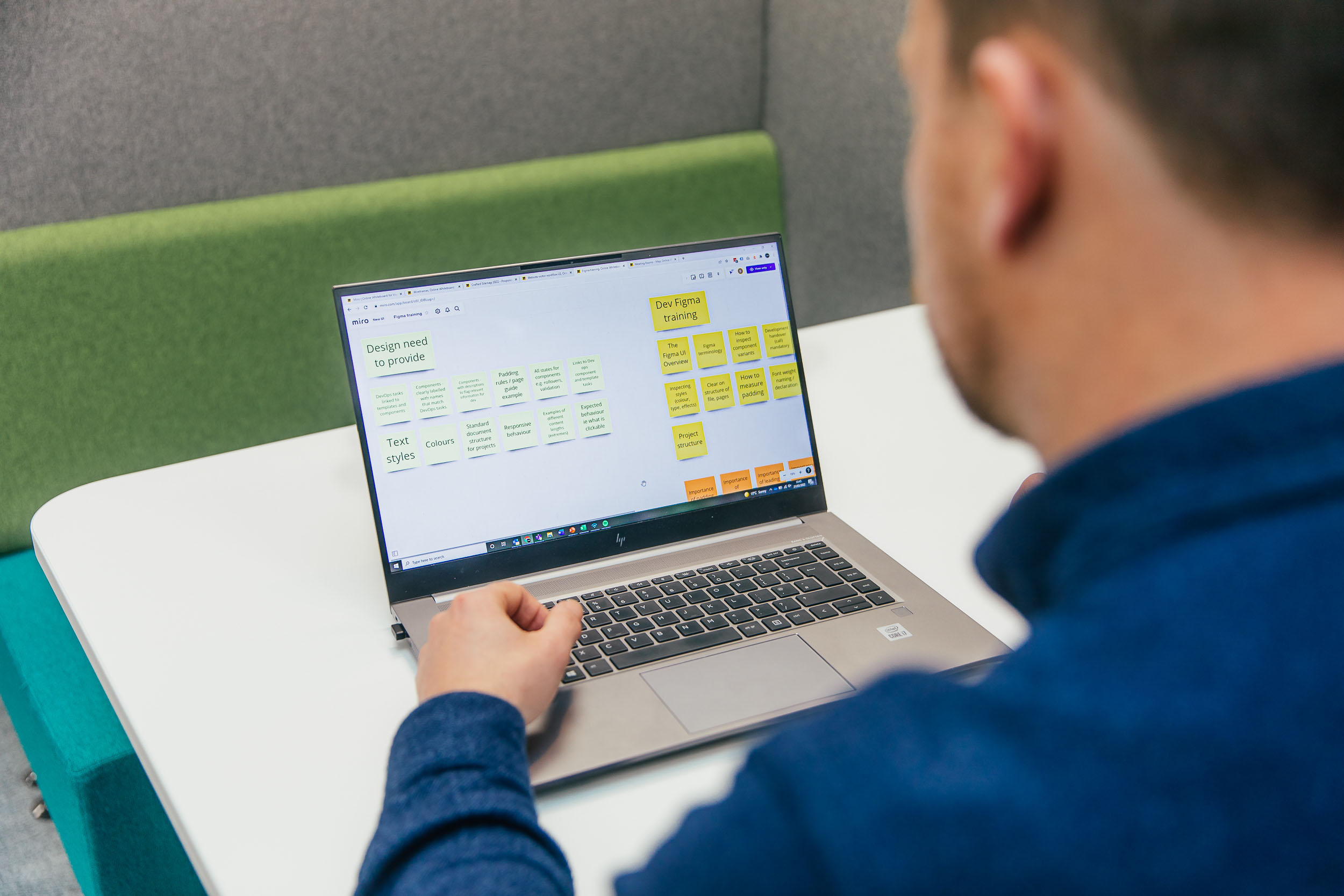 An over the shoulder shot of someone on a laptop. The screen shows a list of tasks for a designer. 