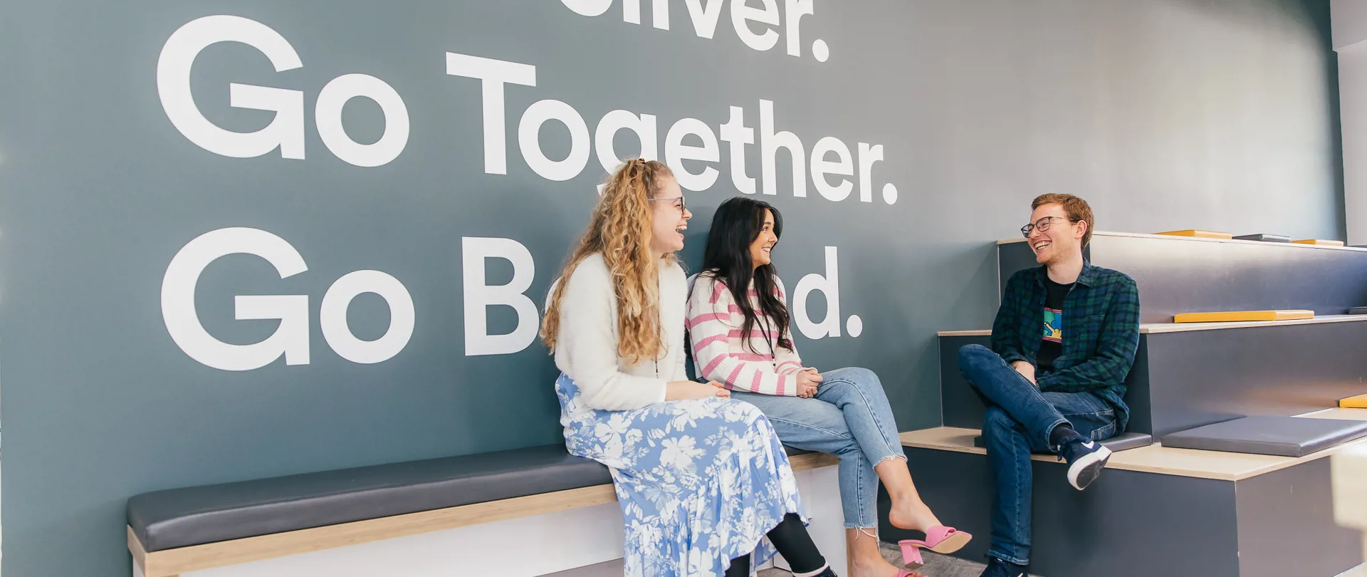 Crafted team talking in front of company values wall graphic saying Go Deliver, Go Together, Go Beyond